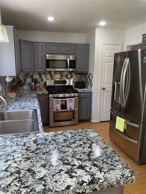 10702 Allens Landing Dr, Houston, TX 77065 - kitchen with stainless steel appliances, a sink, gray cabinetry, a textured ceiling, and backsplash