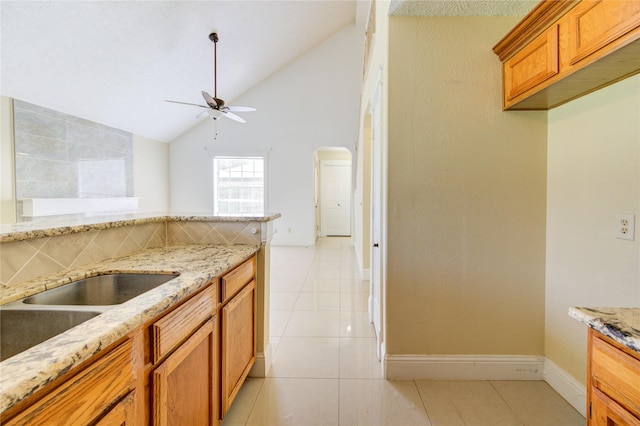 2815 Lakefield Way, Sugar Land, TX 77479 - kitchen with ceiling fan, brown cabinetry, lofted ceiling, light tile patterned floors, and light stone counters