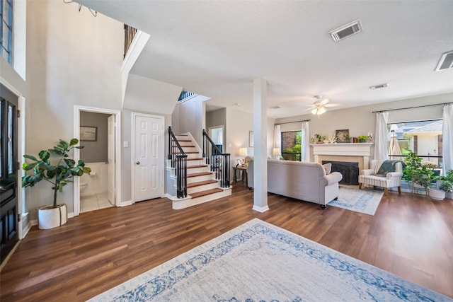 living area with wood finished floors, stairs, a fireplace, a ceiling fan, and baseboards