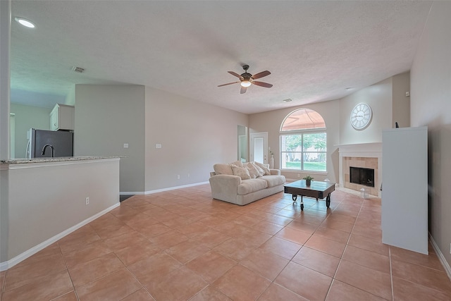 21122 Lilac Meadows Ln, Richmond, TX 77407 - living room with a ceiling fan, a tile fireplace, a textured ceiling, light tile patterned flooring, and baseboards