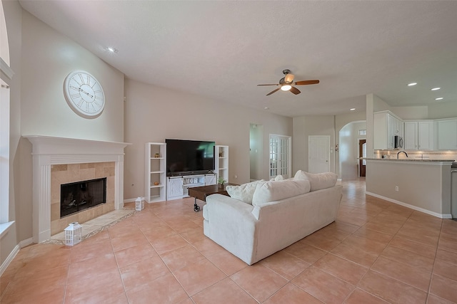 21122 Lilac Meadows Ln, Richmond, TX 77407 - living room featuring ceiling fan, light tile patterned floors, arched walkways, a tiled fireplace, and recessed lighting