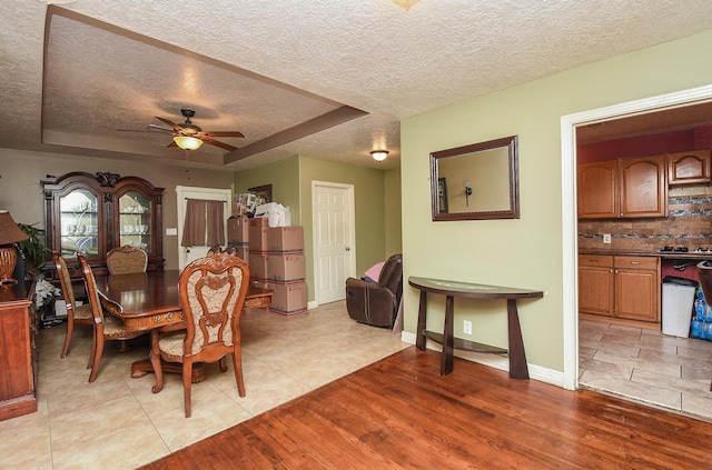 130 Ben Dr, Houston, TX 77022 - dining room featuring a textured ceiling, light wood finished floors, a ceiling fan, a tray ceiling, and baseboards