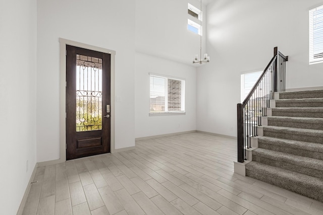 foyer with stairs, a chandelier, plenty of natural light, light wood-style floors, and a towering ceiling