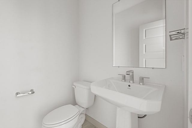 half bath with toilet, a sink, baseboards, and tile patterned floors