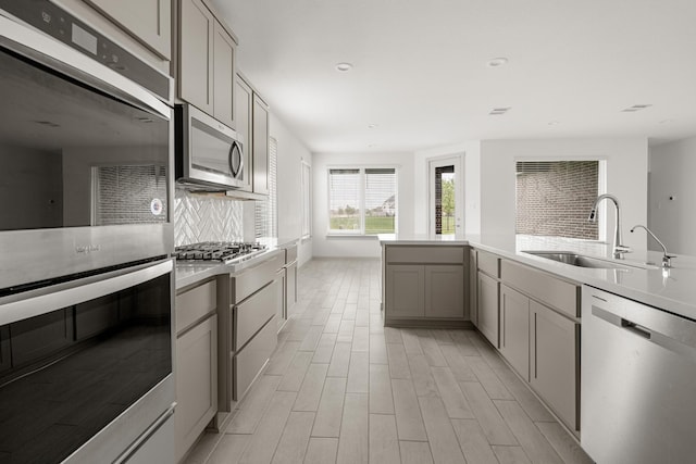 kitchen with appliances with stainless steel finishes, a sink, gray cabinetry, decorative backsplash, and light wood-style flooring