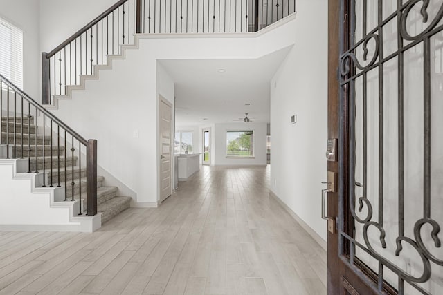 entryway with a towering ceiling, wood finished floors, stairway, baseboards, and a ceiling fan