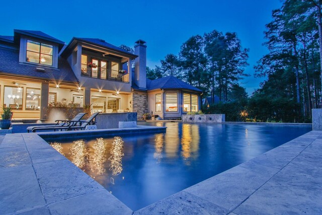 28842 Lakeside Grn, Magnolia, TX 77355 - back of house at night featuring a ceiling fan, a balcony, a chimney, an outdoor pool, and a patio