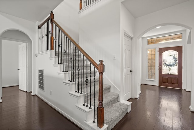 entryway with arched walkways, dark wood finished floors, and baseboards