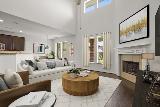 living area with plenty of natural light, dark wood finished floors, a tile fireplace, recessed lighting, and a high ceiling