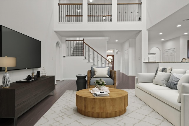 living area featuring arched walkways, a high ceiling, stairs, wood finished floors, and recessed lighting