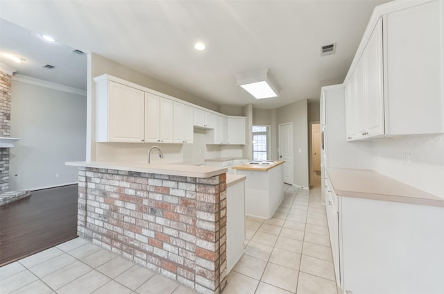 12950 Quail Park Dr, Cypress, TX 77429 - kitchen with light tile patterned floors, a peninsula, ornamental molding, light countertops, and white cabinetry