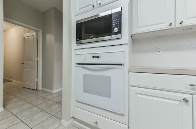 12950 Quail Park Dr, Cypress, TX 77429 - kitchen featuring white oven, stainless steel microwave, white cabinets, light tile patterned floors, and baseboards