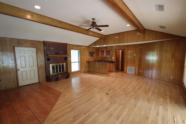 606 County Road 1947, Yantis, TX 75497 - unfurnished living room featuring wood walls, a ceiling fan, light wood-style flooring, and a brick fireplace