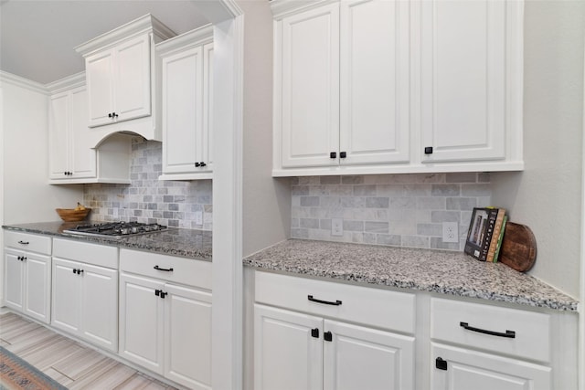 kitchen with backsplash, white cabinets, light stone counters, and stainless steel gas stovetop