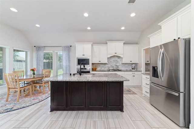 kitchen featuring appliances with stainless steel finishes, vaulted ceiling, backsplash, white cabinetry, and a center island with sink
