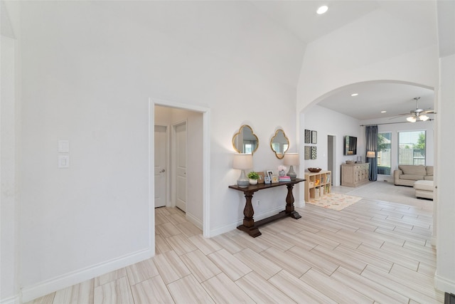 hallway with arched walkways, baseboards, a high ceiling, and recessed lighting