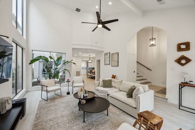 living area with stairway, light wood-style floors, high vaulted ceiling, ceiling fan, and beam ceiling