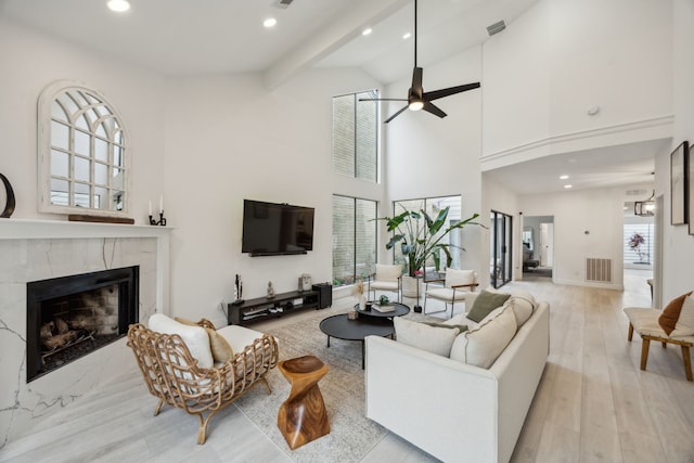 living room with a high end fireplace, high vaulted ceiling, ceiling fan, recessed lighting, and light wood-style flooring