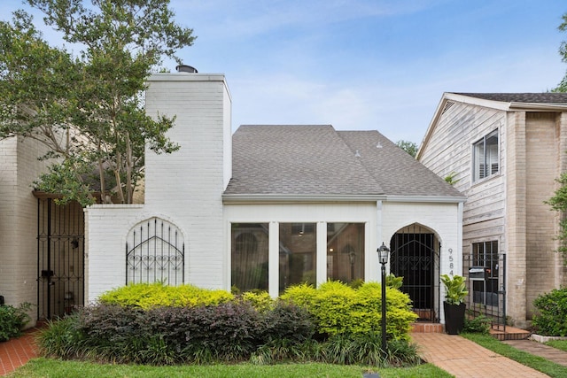 view of front of house with a gate, roof with shingles, a chimney, and brick siding