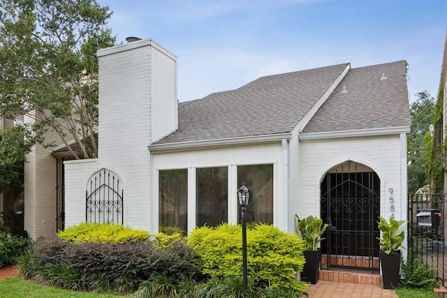 view of front of home with brick siding, a shingled roof, a chimney, and fence