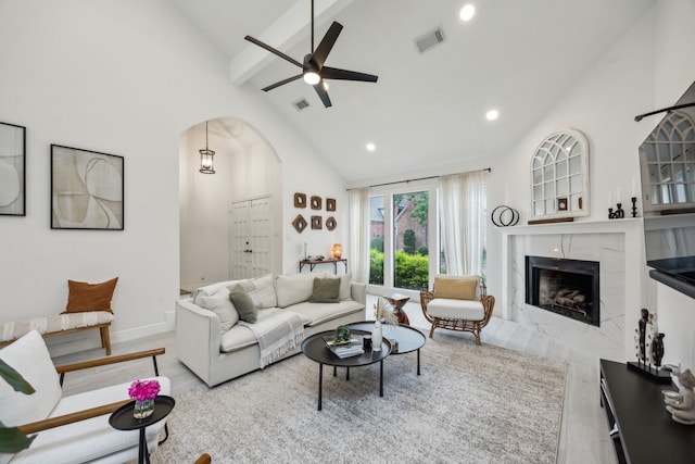 living area featuring high vaulted ceiling, beamed ceiling, a high end fireplace, a ceiling fan, and arched walkways