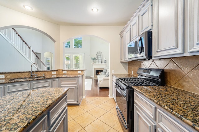 11018 Jadestone Creek Ln, Cypress, TX 77433 - kitchen with stainless steel appliances, a sink, backsplash, dark stone counters, and a warm lit fireplace