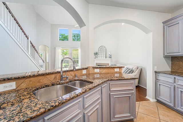 11018 Jadestone Creek Ln, Cypress, TX 77433 - kitchen with a sink, dark stone countertops, arched walkways, light tile patterned flooring, and a towering ceiling