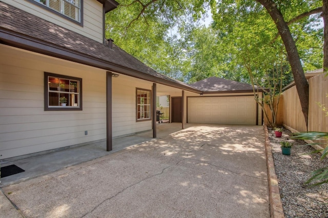 view of side of property with fence, concrete driveway, a shingled roof, and a garage