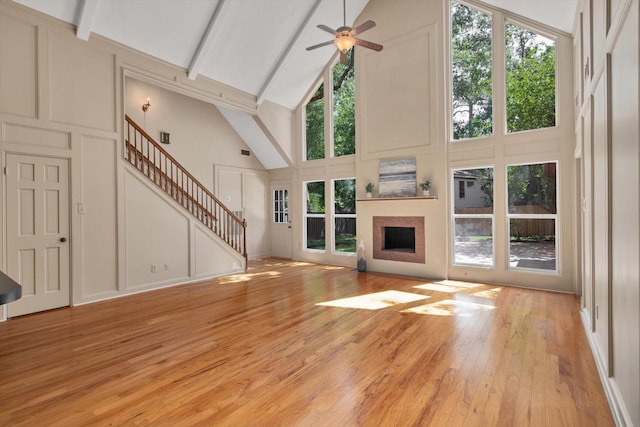 unfurnished living room with a decorative wall, high vaulted ceiling, stairway, a ceiling fan, and a fireplace