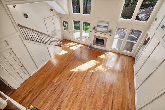 unfurnished living room with light wood-style floors, a high ceiling, a tiled fireplace, and stairway