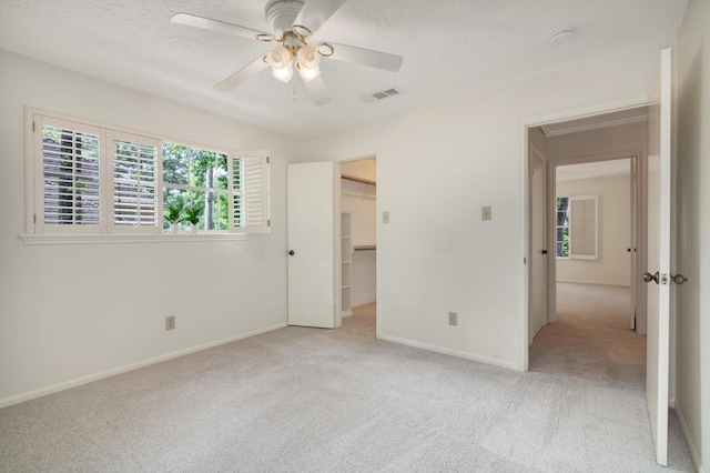 unfurnished bedroom with light colored carpet, baseboards, a ceiling fan, a textured ceiling, and a walk in closet