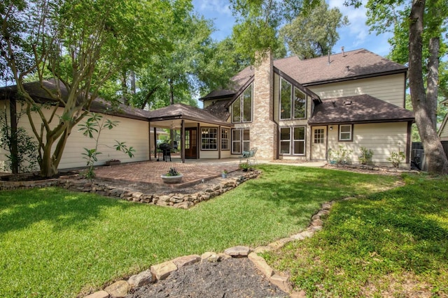 rear view of house featuring a patio, a lawn, a chimney, and a shingled roof