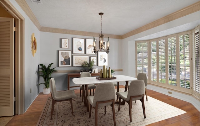 dining space featuring a chandelier, wood finished floors, a textured ceiling, crown molding, and baseboards