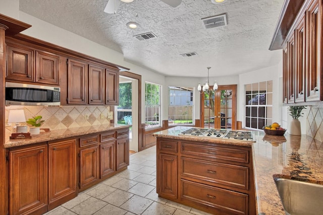 kitchen with appliances with stainless steel finishes, decorative backsplash, a chandelier, a peninsula, and light stone countertops