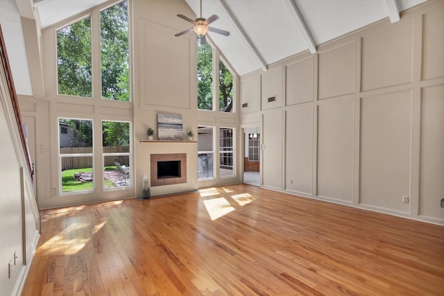 unfurnished living room with a decorative wall, high vaulted ceiling, light wood-type flooring, healthy amount of natural light, and a ceiling fan