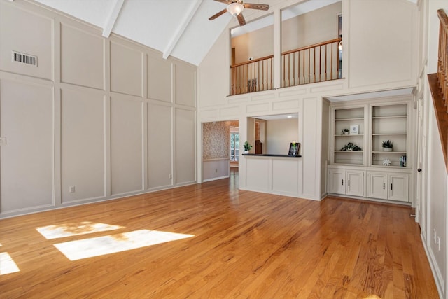 unfurnished living room with a decorative wall, high vaulted ceiling, ceiling fan, light wood finished floors, and beamed ceiling