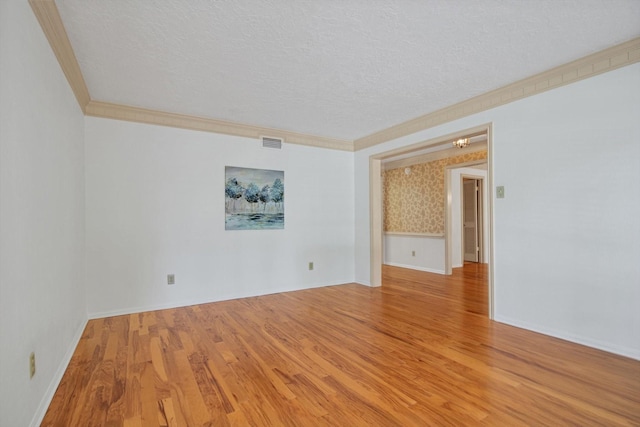 spare room with a textured ceiling, wood finished floors, ornamental molding, and baseboards