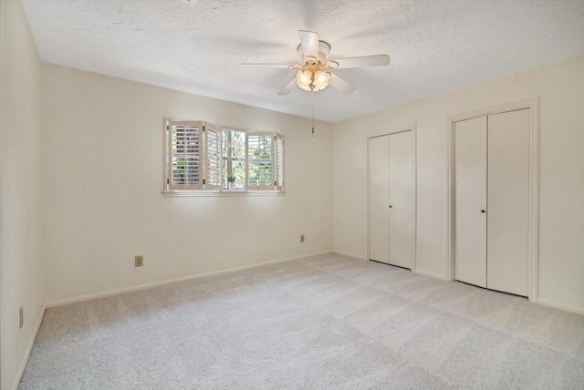 unfurnished bedroom featuring a textured ceiling, two closets, light carpet, baseboards, and ceiling fan