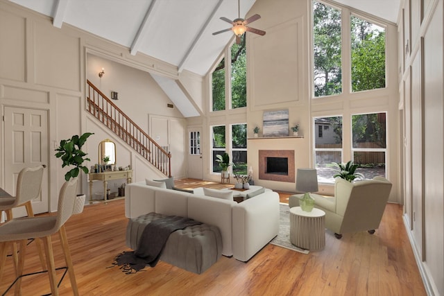 living room featuring high vaulted ceiling, a decorative wall, a fireplace, stairway, and a ceiling fan