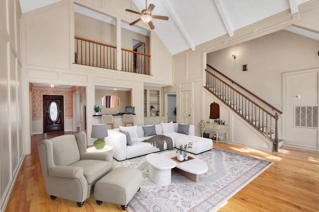living area with a decorative wall, stairs, high vaulted ceiling, ceiling fan, and wood finished floors