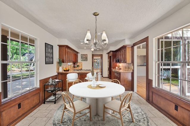 dining area with a chandelier, a textured ceiling, a wainscoted wall, and stone tile floors