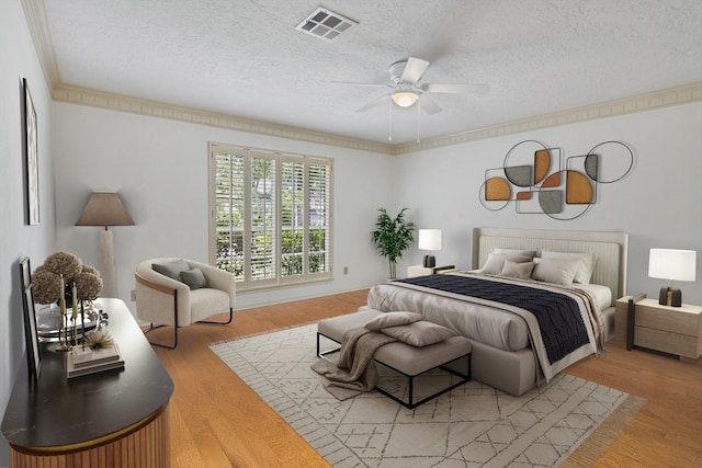 bedroom featuring a textured ceiling, light wood-type flooring, ceiling fan, and ornamental molding