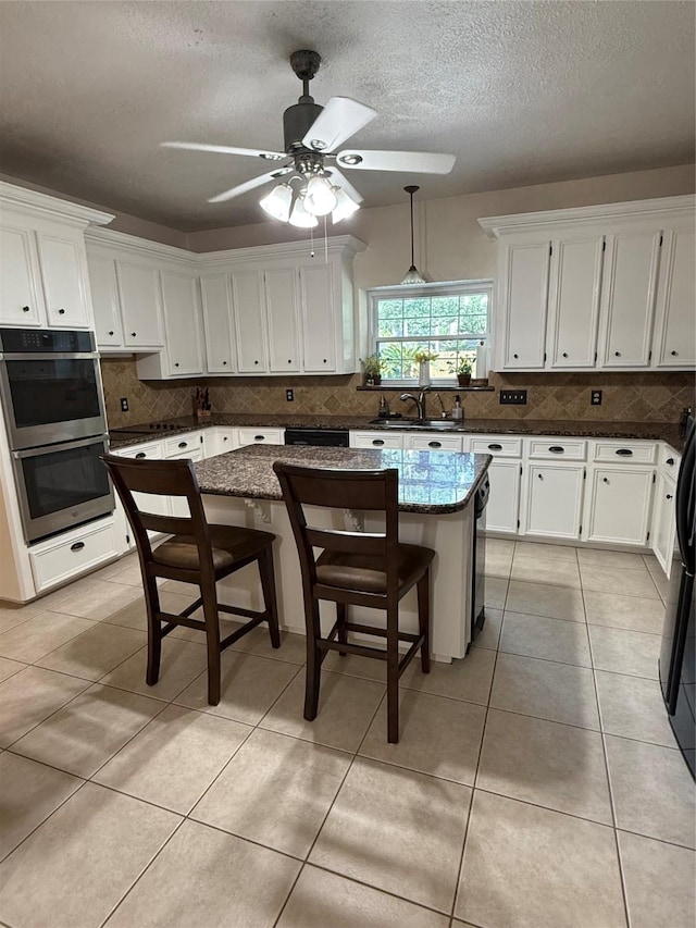 13102 Lake Mist Dr, Cypress, TX 77429 - kitchen with double oven, white cabinets, tasteful backsplash, ceiling fan, and a textured ceiling