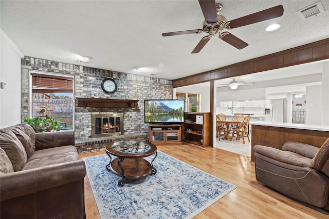 231 Corpus Dr, Magnolia, TX 77354 - living room featuring a textured ceiling, a ceiling fan, light wood finished floors, a brick fireplace, and crown molding
