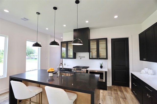 609 E 38th St, Houston, TX 77022 - kitchen with a sink, light wood-type flooring, dark cabinets, glass insert cabinets, and recessed lighting