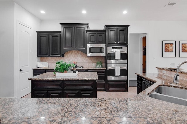 11307 Bentgrove Ln, Cypress, TX 77433 - kitchen with stainless steel appliances, a sink, dark cabinetry, tasteful backsplash, and light stone counters