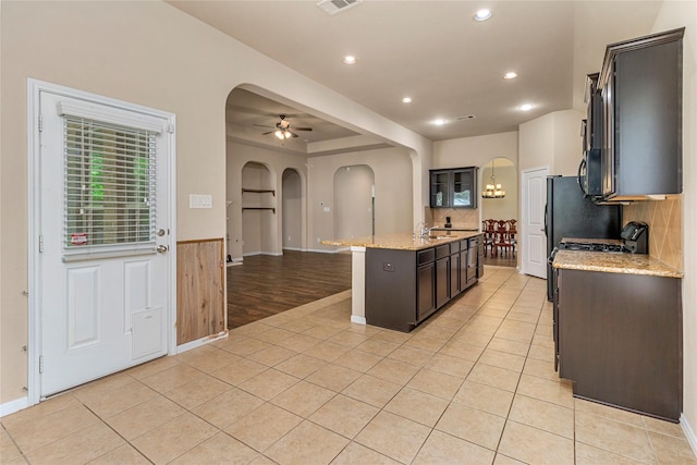 1938 Honey Laurel Dr, Conroe, TX 77304 - kitchen featuring arched walkways, a ceiling fan, light tile patterned flooring, an island with sink, and light stone counters