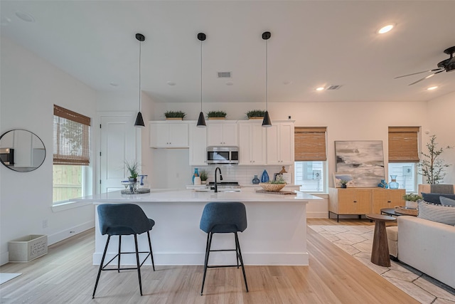 2706 Bostic St, Houston, TX 77093 - kitchen with stainless steel microwave, white cabinets, a kitchen island with sink, decorative backsplash, and light wood-style flooring