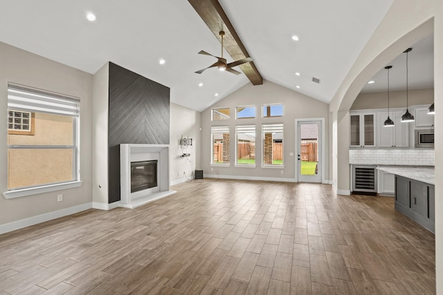 10630 Hazel Hills Dr, Cypress, TX 77433 - unfurnished living room featuring ceiling fan, wine cooler, beamed ceiling, plenty of natural light, and a glass covered fireplace