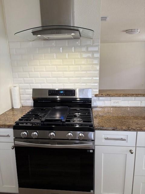 3213 Whitesail Dr, League City, TX 77573 - kitchen featuring stainless steel gas stove, wall chimney exhaust hood, backsplash, white cabinets, and dark stone countertops